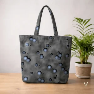 Nebula Droplets AOP Designer Large Tote Bag by VertexVault Studio, showing a smoky dark grey cosmic pattern shoulder bag with 3D blue-grey droplets on a wooden table next to a potted plant.